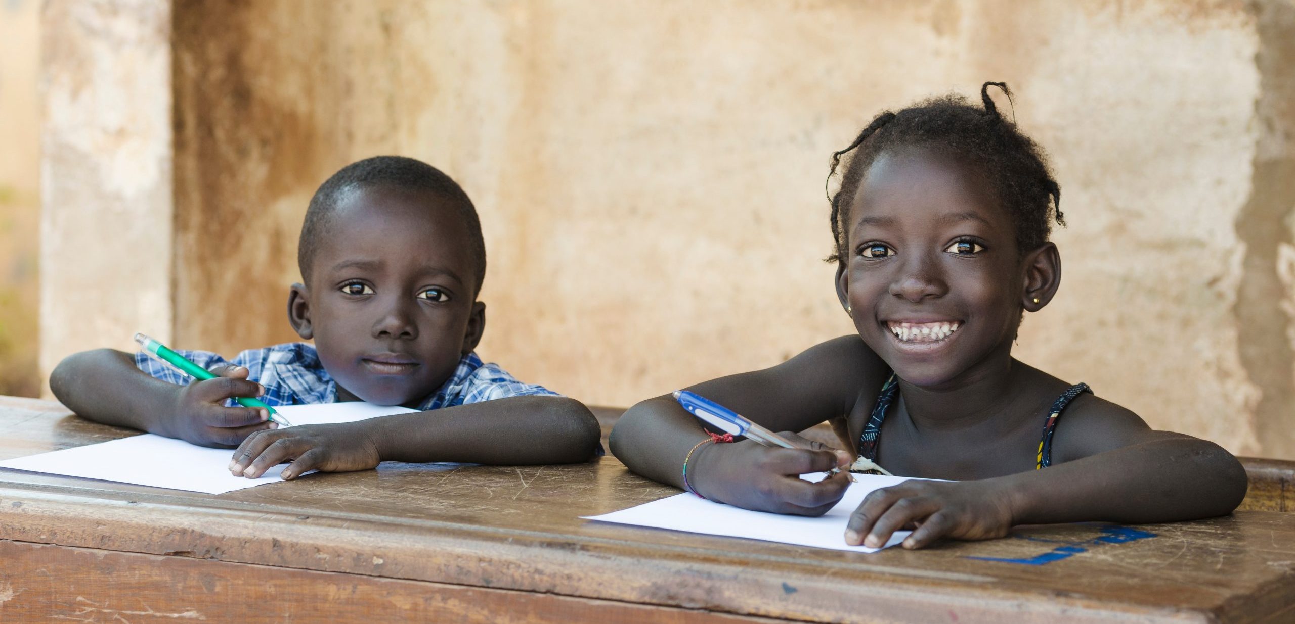 Two children sitting at a desk with paper and writing implements in Mali, Africa